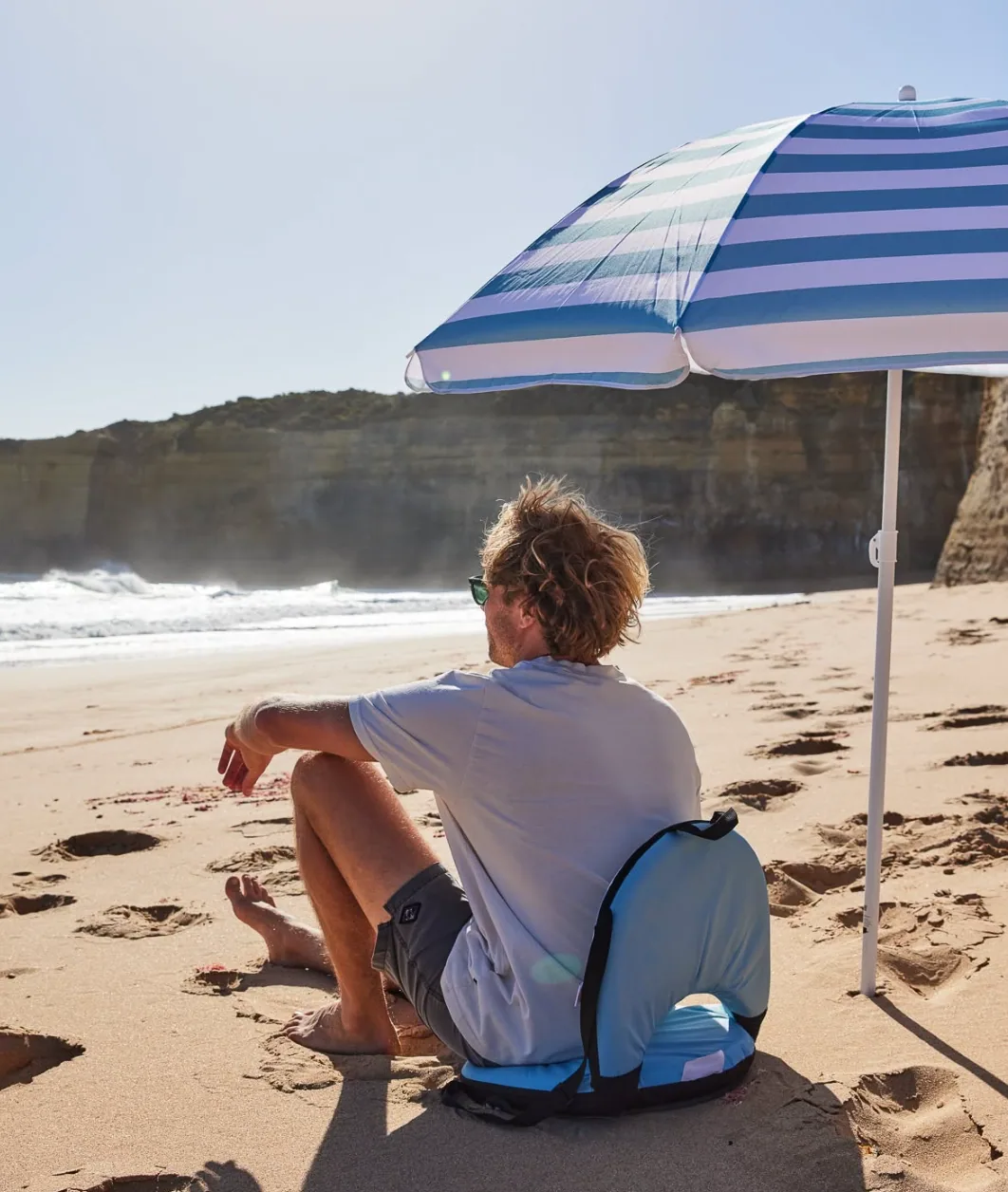 Relaxing on the beach beneath a blue striped umbrella