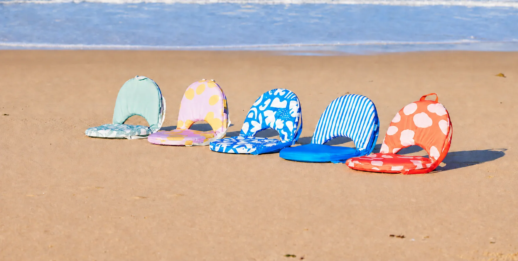 Five colourful folding beach chairs lined up on the sand beside the ocean
