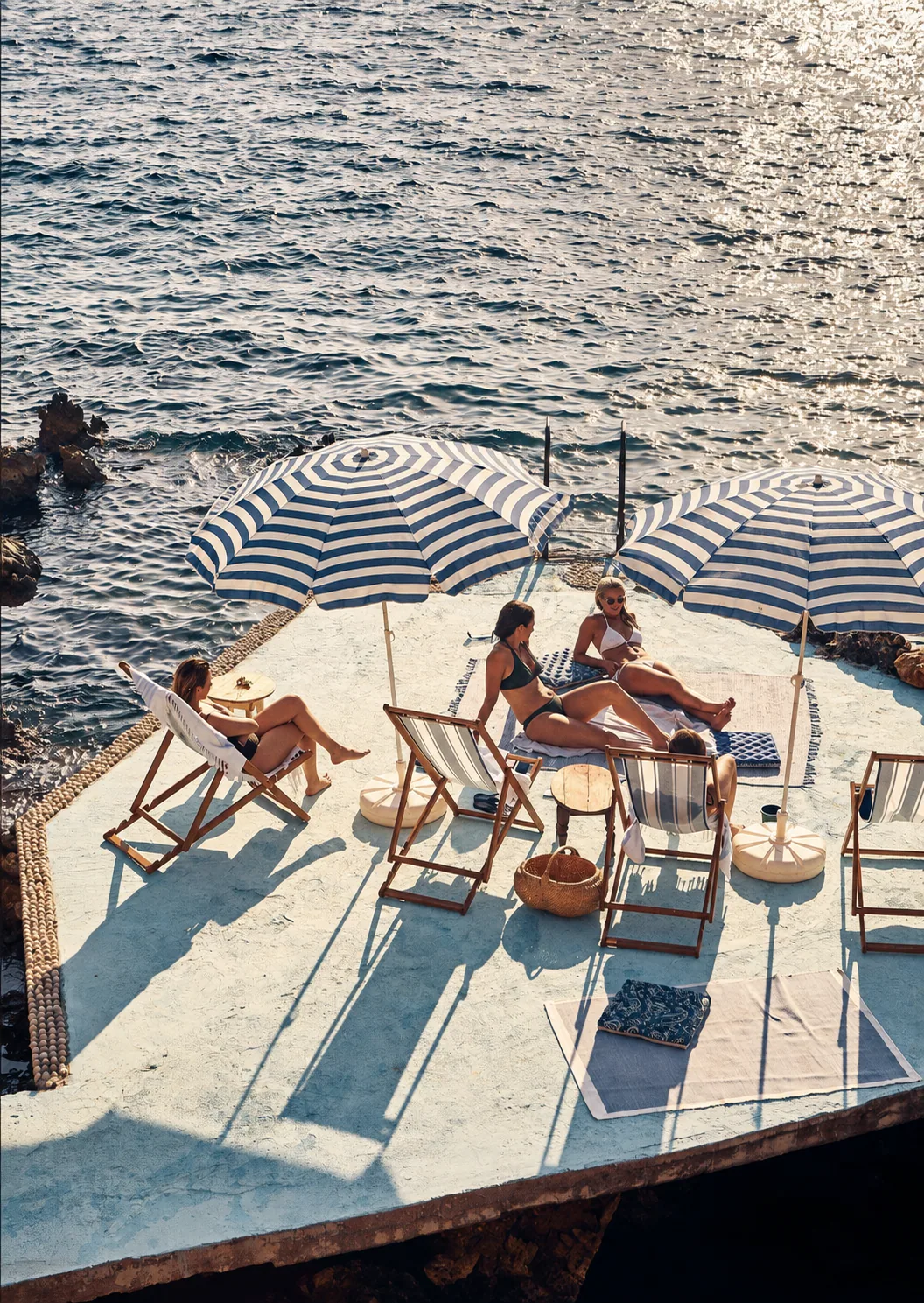 Blue and white beach umbrellas and deck chairs beside sunlit coastal waters