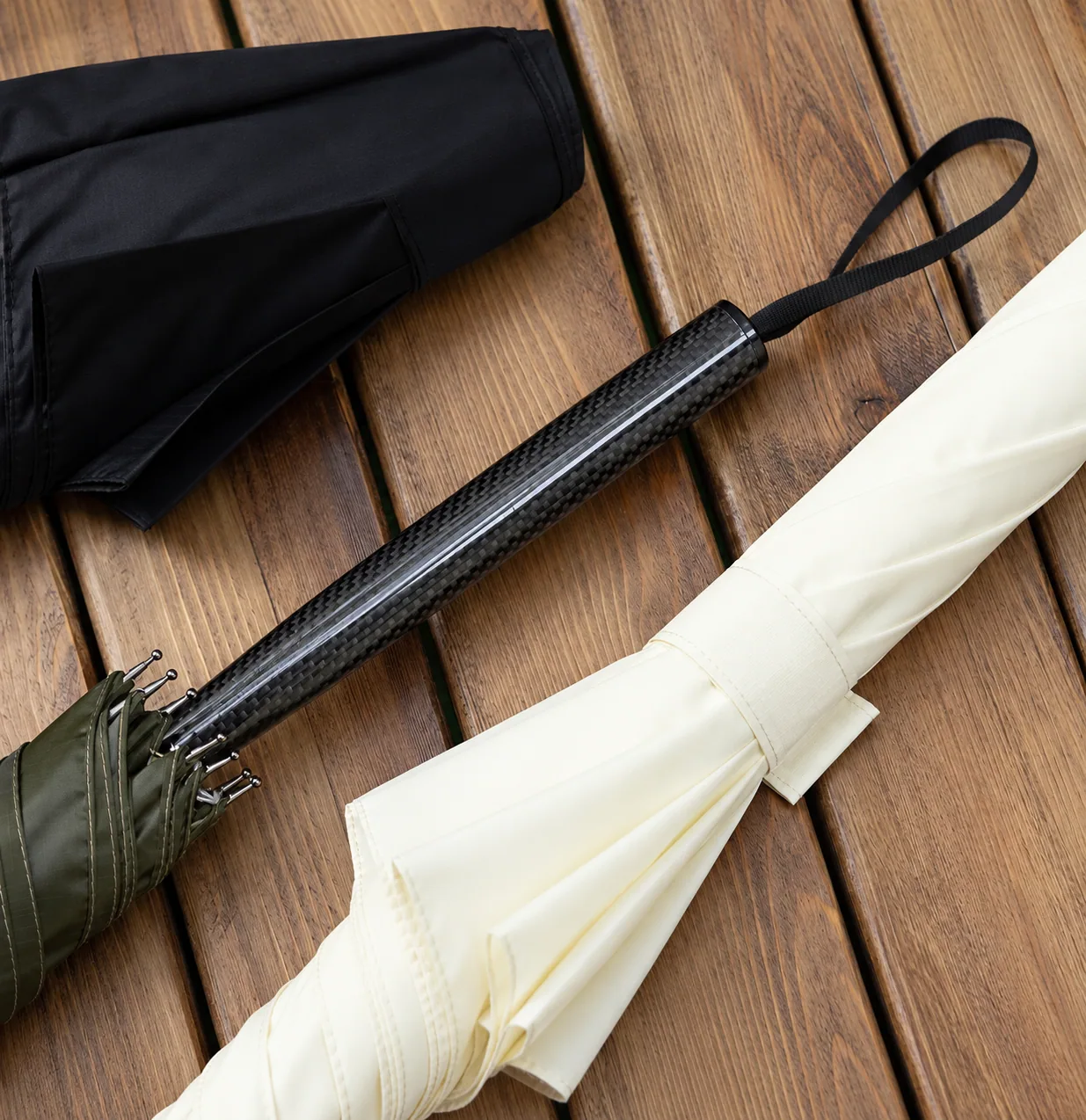 Straight carbon-fibre handle and wrist strap beside closed umbrellas
