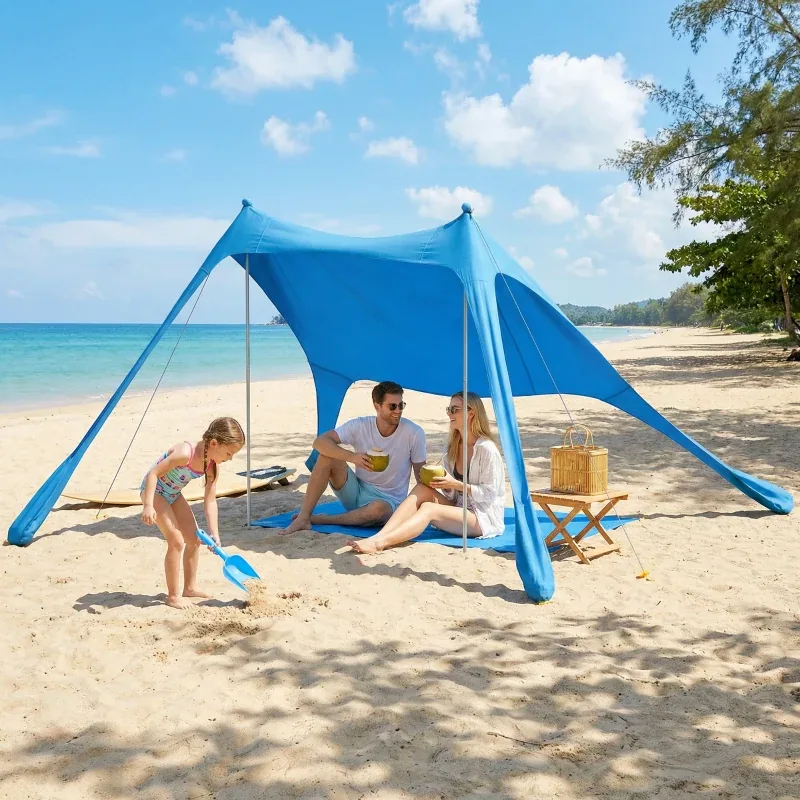 Family enjoying shade beneath a light blue beach tent beside the sea